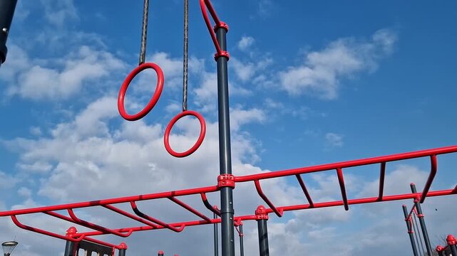 Gymnastic rings for the street. Open-air sports grounds. Red pull-up rings on the sky background. Public space for training. Concept of physical activity development. Zones for various exercises