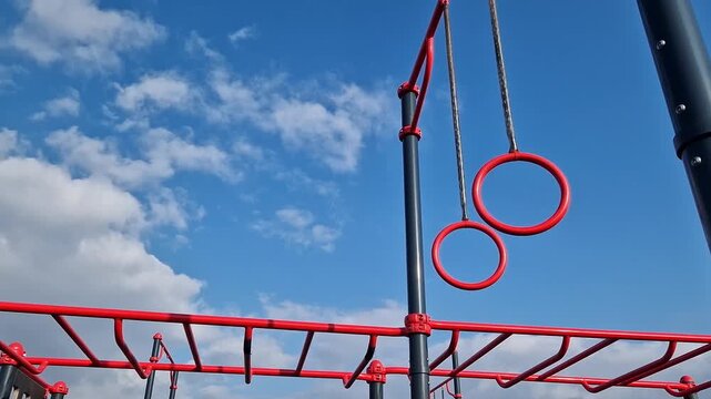 Gymnastic rings for the street. Open-air sports grounds. Red pull-up rings on the sky background. Public space for training. Concept of physical activity development. Zones for various exercises