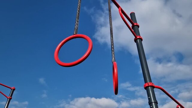 Gymnastic rings for the street. Open-air sports grounds. Red pull-up rings on the sky background. Public space for training. Concept of physical activity development. Zones for various exercises