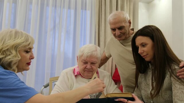 Senior woman sitting at a table sharing memories with her son and daughters while looking together at an old family photo album, reminiscing about the past and celebrating their bond