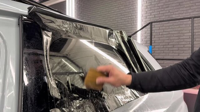 Technician Installing car window tint. Window toned film. Car window tinting specialist install car film windscreen. Applying tinting foil on a window in the detailing studio. Concept of love cars. 