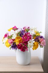 Naklejka premium Beautiful freesia flowers in vase on wooden table near white wall indoors, closeup