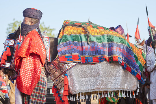 Argugun, Nigeria - 13 February 2026: View of a man in traditional attire, his red robe a stark contrast to the shimmering silver of the horse's ornate covering.