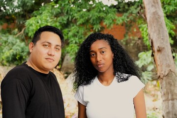 Fototapeta premium Authentic and romantic moments of a young diverse couple sharing affection and spending quality time together in a lush outdoor garden setting during a bright day 