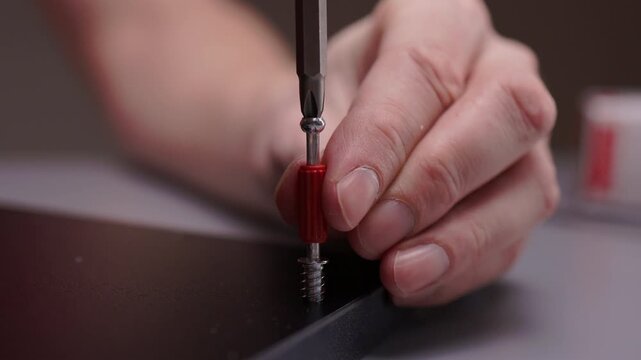 Close-up hand of handyman using electric screwdriver to tighten screw into dark surface, performing assembly work and showcasing precision, diy skills, home improvement, close-up, slow motion.