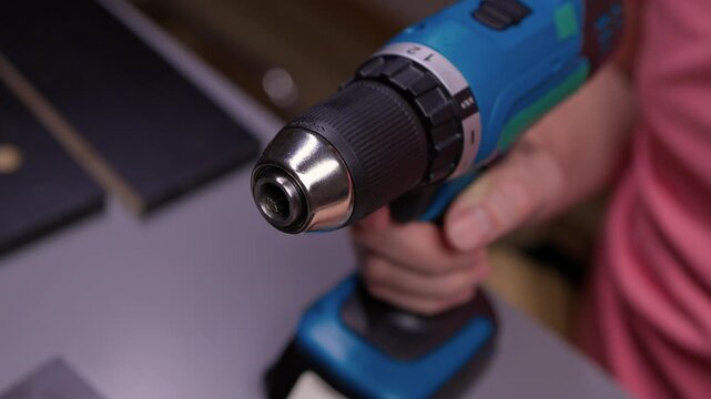 Worker hands replacing sanding disc with head bit on cordless electric screwdriver, preparing tool for furniture assembly or repair tasks, close-up, slow motion. Concept of household chores.