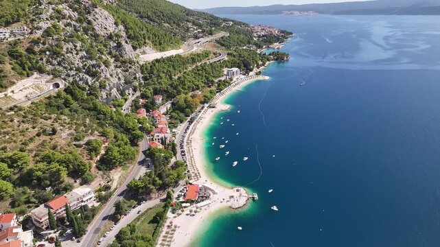 Drone aerial view of long sandy beaches in Omis with clear turquoise Adriatic sea and scenic Dalmatian coastline.