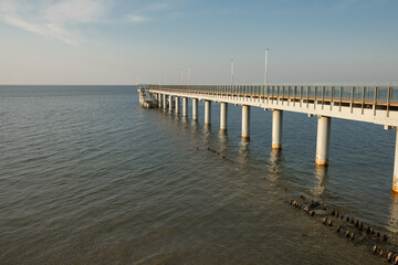 Fototapeta premium Long wooden pier extending over calm water with clear blue sky and distant horizon, ideal for scenic views and relaxation