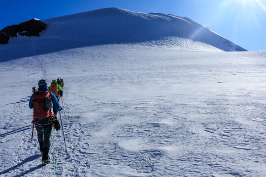 Mountaineers in rope team with crampons ascending towards mountain summit Parrotspitze and glacier panorama in the morning in Pennine Alps, Italy