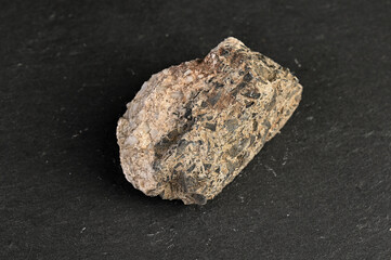 Fototapeta premium Close-up of a rough, textured igneous rock specimen with visible mineral inclusions on a dark background