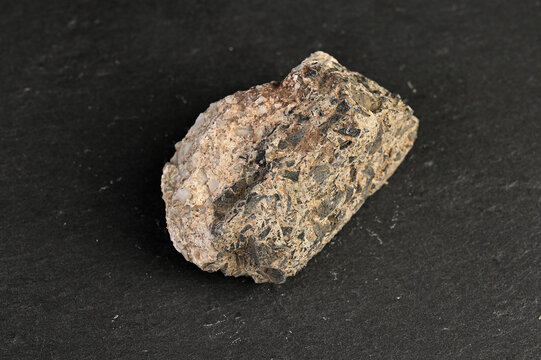 Close-up of a rough, textured igneous rock specimen with visible mineral inclusions on a dark background