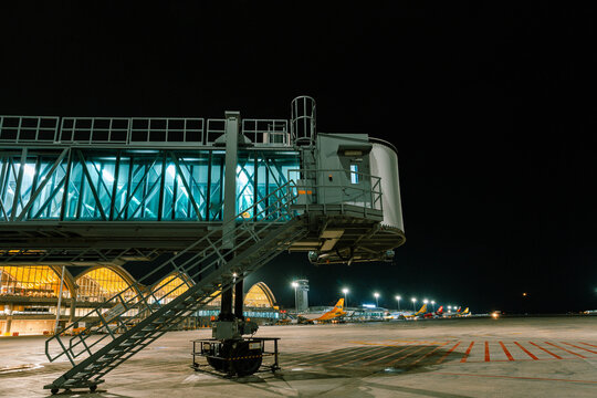 Lapu-Lapu, Philippines - 20 July 2018: View of a jet bridge bathed in cool blues against the warm glow of the airport terminal at night.