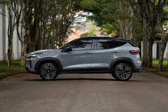 Grey Fiat Pulse Abarth side profile view on tree lined road, compact SUV on empty paved street 