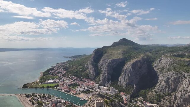 Drone aerial view of Fortica fortress above Omi&scaron; with Cetina river flowing into Adriatic sea surrounded by steep mountains and coastal scenery