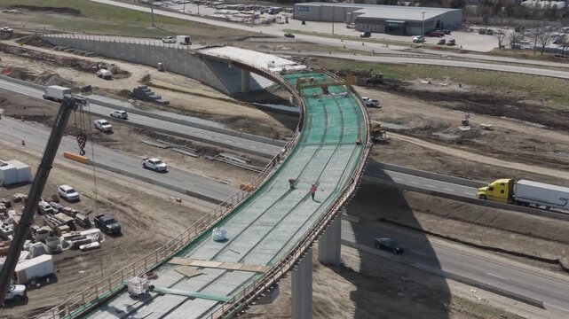 Denton, Texas USA &ndash; February 18, 2026: Construction workers on an elevated bridge ramp under construction at a highway interchange with vehicles traveling on surrounding roadways.