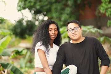 Obraz premium Authentic and romantic moments of a young diverse couple sharing affection and spending quality time together in a lush outdoor garden setting during a bright day 