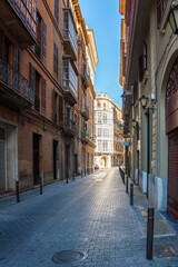 Fototapeta premium Narrow old town street in Palma with historic facades, balconies, and a view of a bright corner building.