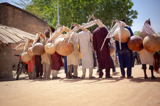 Argungu, Nigeria - 12 February 2026: View of men carrying gourds in a procession, their silhouettes stark against the backdrop of buildings and a dusty ground, a vibrant cultural display.