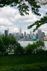 Obraz premium View of New York City skyline with Empire State Building from park during daytime under partly cloudy sky