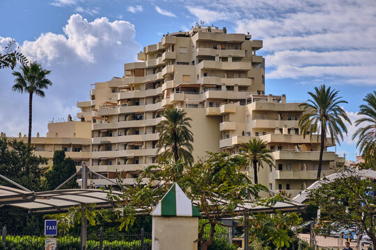 Benalmadena, Spain - 24 December 2025: View of the distinctive architecture of the Hotel Alay, its staggered balconies catching the sunlight amidst the city's lush greenery and blue skies.