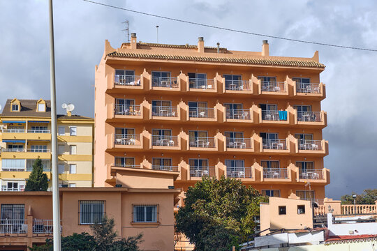 Benalmadena, Spain - 24 December 2025: View of a multi-story peach-colored building with repetitive balconies creating a rhythmic pattern against the sky.