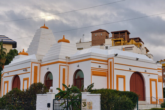 Benalmadena, Spain - 23 December 2025: View of the Hindu Temple's white walls contrasting against the orange trim under a cloudy sky, surrounded by lush greenery.