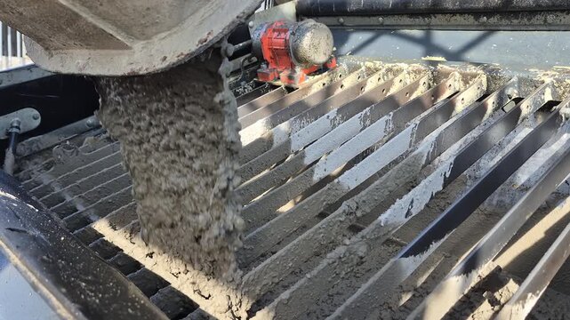 Close up diagonal rear view of a concrete mixer truck pouring fresh cement into a concrete pump hopper on a construction site.