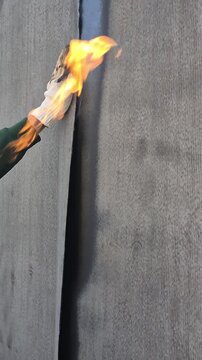 Vertical 9:16 slow motion diagonal shot of a worker's hand smoothing a hot bituminous membrane behind a gas torch flame during foundation waterproofing.