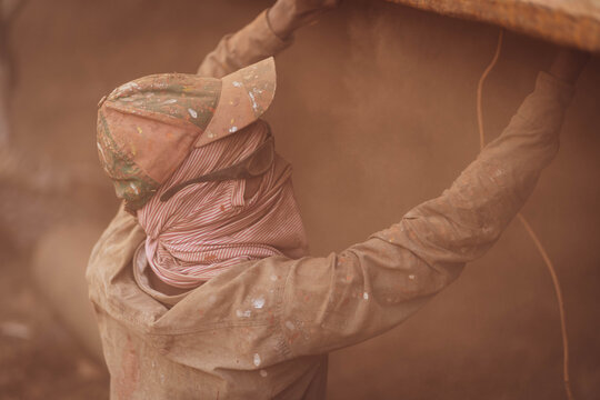 Keraniganj, Bangladesh - 11 February 2023: View of a worker shrouded in dust, lifting heavy construction material, the scene a monochrome study in browns and tans.