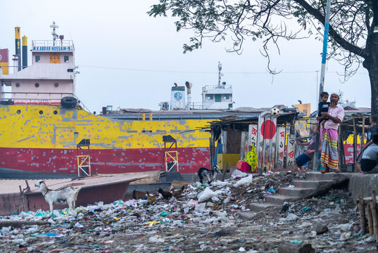 Keraniganj, Bangladesh - 13 December 2023: View of the riverbank where vibrant yellow and red barges contrast with the muted tones of the dwellings.