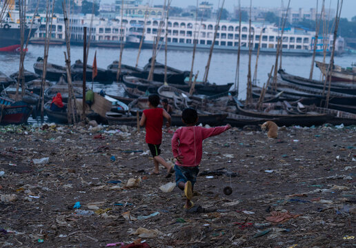 Keraniganj, Bangladesh - 13 December 2023: View of children running barefoot across the littered riverbank near the boats, a scene of resilience amidst the rough textures.