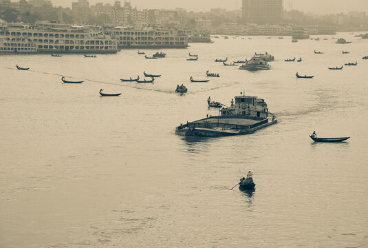 Keraniganj, Bangladesh - 23 September 2022: View of the river bustling with an array of boats, from small canoes to larger barges, against the backdrop of the city's skyline.