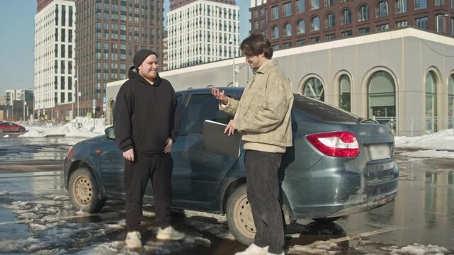 Man buys a used car from private seller as the owner hands him the car keys on a winter parking lot.
