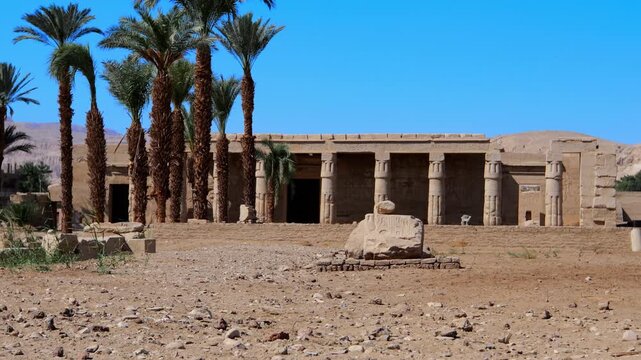 Seti I mortuary temple exterior with Osiride colonnade and palm trees in Luxor Egypt. Ancient sandstone ruins in desert landscape.