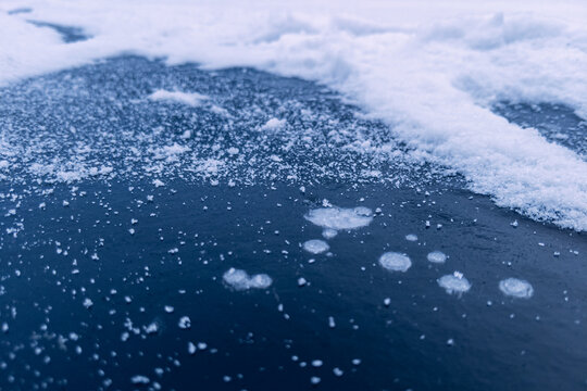 Blue frozen pond ice sprinkled with fresh snow crystals and bubbles