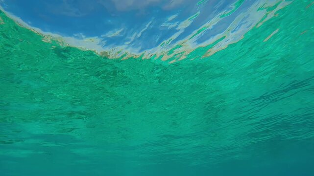 View from below of the emerald green water surface with blue sky in shallow water during the doldrums. Natural underwater background of calm water surface with fine ripples