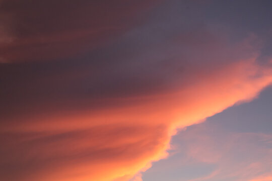 Dramatic sunset cloud formation with fiery orange light contrasting against dark purple and blue storm clouds