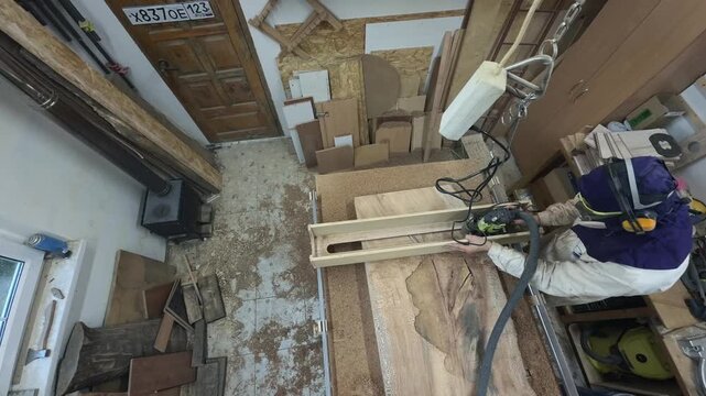 Overhead Swivel Pan of Unrecognizable Carpenter in Extreme Safety Gear Surfacing Raw Walnut Slab with Router Authentic Cluttered Workshop Slow Motion