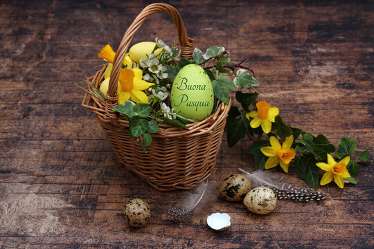 Auguri di Pasqua italiani "Buona Pasqua" su un uovo verde in un cestino di vimini con narcisi gialli e uova di quaglia.