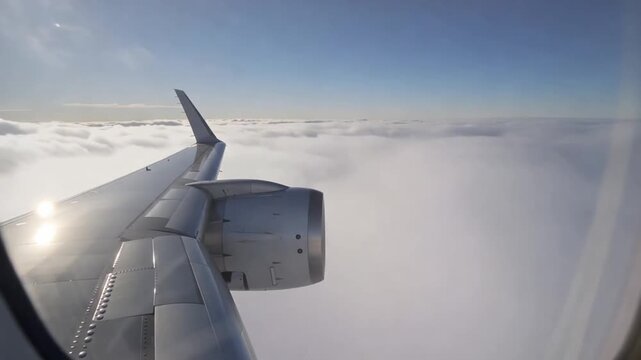 Airplane wing flying above clouds with blue sky background, taken from inside plane