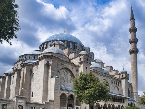 Suleymaniye Mosque Stone Wall View - The majestic S&uuml;leymaniye Mosque domes and minarets tower above a historic stone wall, set against a dramatic, cloudy sky in Istanbul, Turkey.