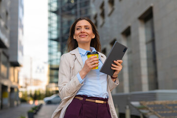 Fototapeta premium Businesswoman walking in city holding coffee and tablet