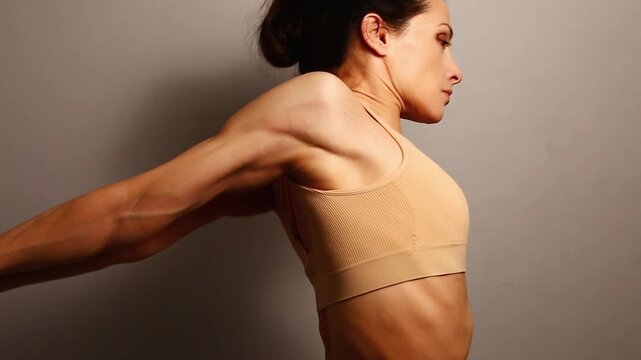 Sport body woman in bra with athletic muscular shoulders and arms doing stretching exercise holding the hands in lock behind the back on studio background with empty copy space. Profile view closeup