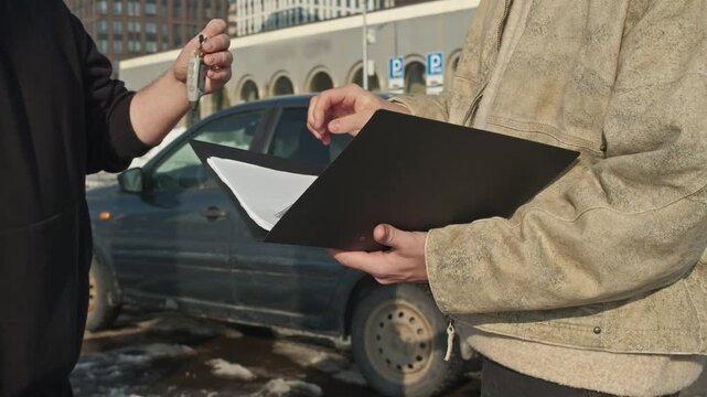 Used car deal: buyer with document folder fills out contract while seller hands him the keys.