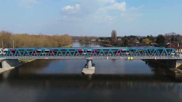 Passenger train crossing blue steel railway bridge over river, aerial frontal view, Czech Republic