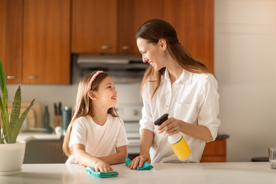 Mother and daughter cleaning kitchen together smiling and bonding, family teamwork and positive parenting concept
