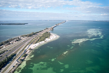 Aerial image of the highway leading up to the Sunshine Skyway Bridge over Tampa Bay linking Pinellas and Manatee County with a small white sand beach pullout for kayakers and boaters