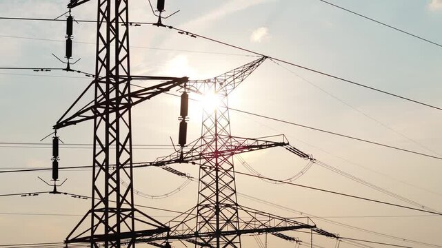 Aerial drone view of electricity pylon silhouette with sun flare behind, power grid infrastructure