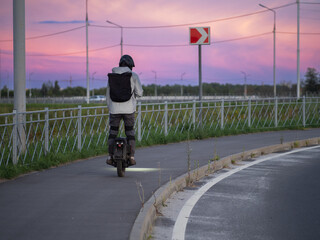 A man on an electric mono wheel rides on the sidewalk. Backpack on the shoulders . A trip home from work © pavelkant