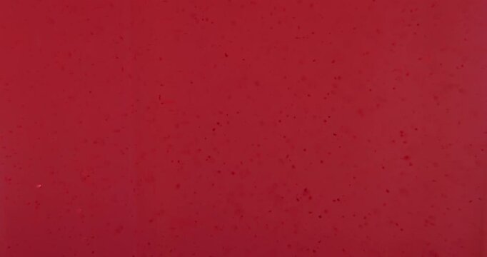 Soft focus close up of pink acrylic paint particles float and diffusing in liquid, forming a gentle abstract texture suitable for creative, beauty, or cosmetic themed designs. Slow motion.